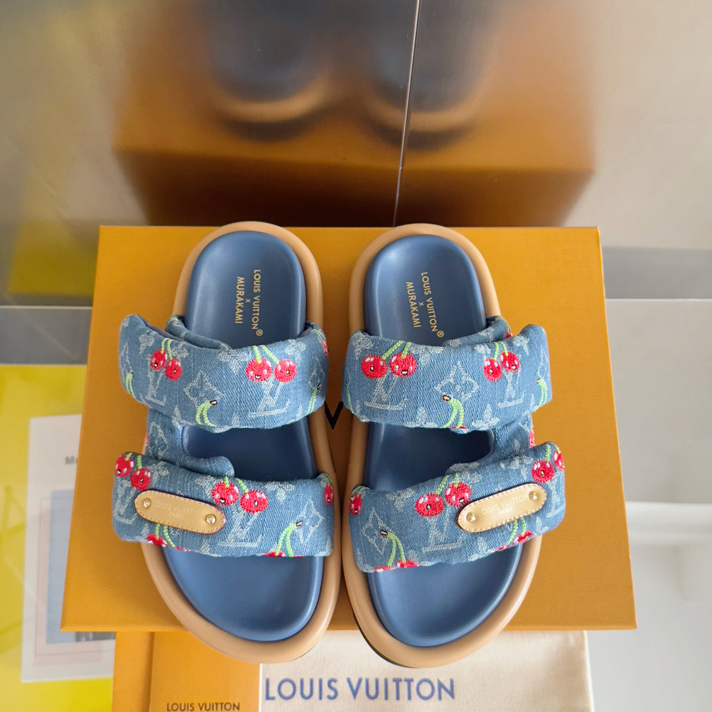 Pair of blue Louis Vuitton slide sandals with cherry print straps and tan buckles