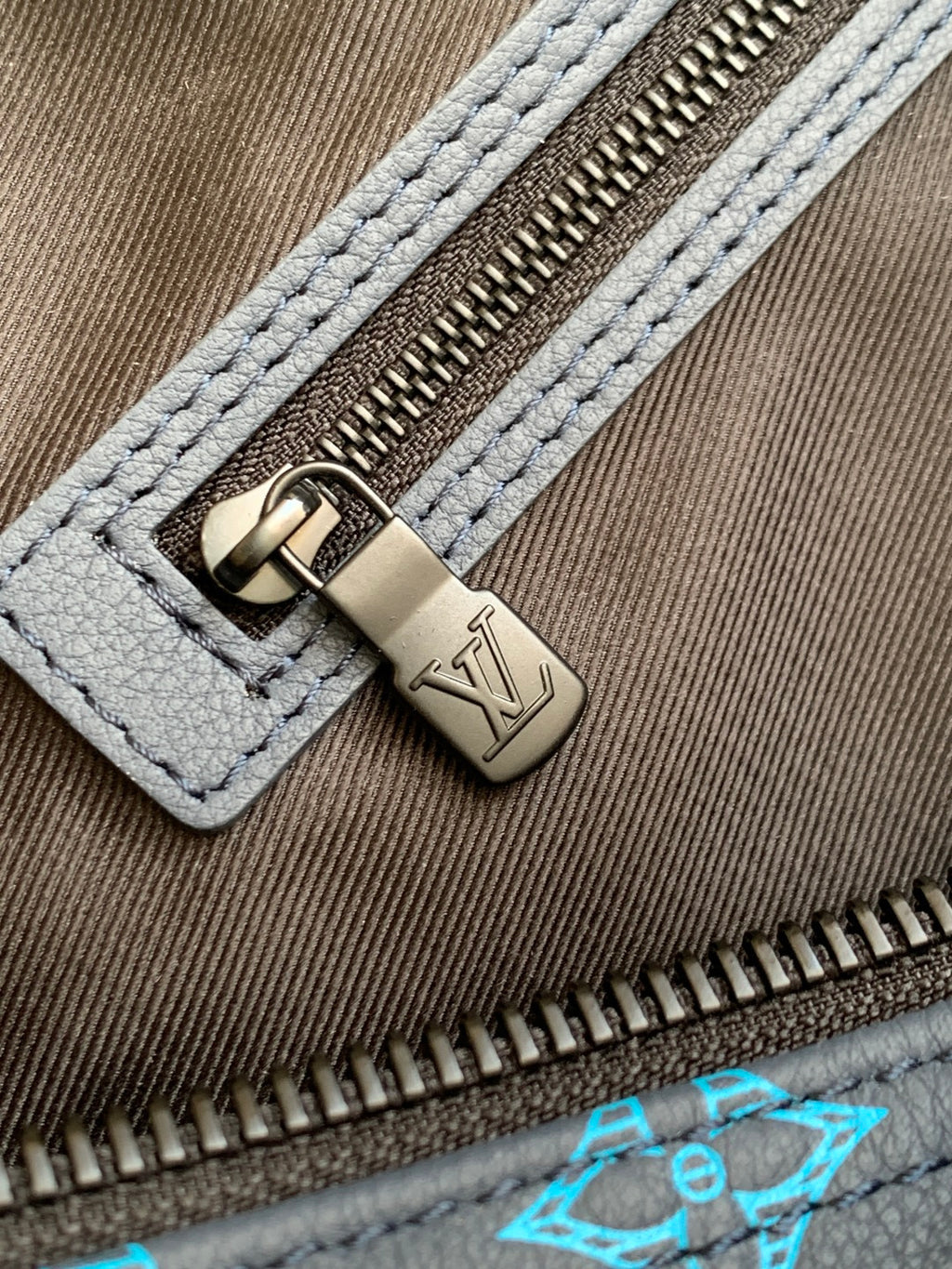 Monogram duffel bag close-up of metal zipper pull on blue canvas edge