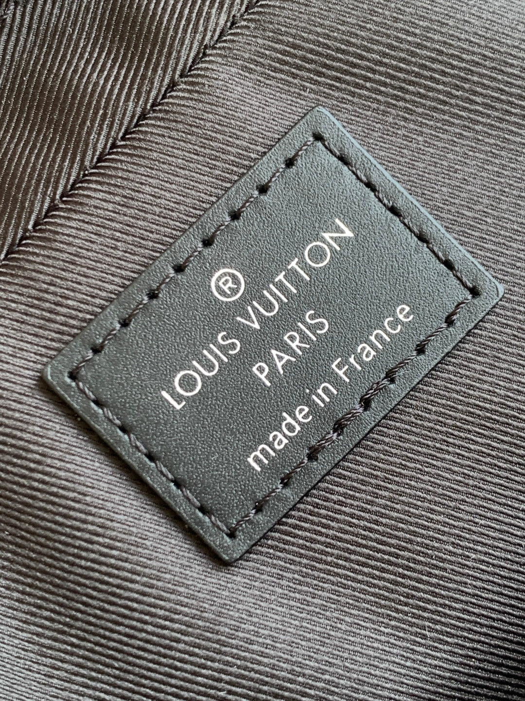 Louis Vuitton label patch on bag with "made in France" text, dark gray leather