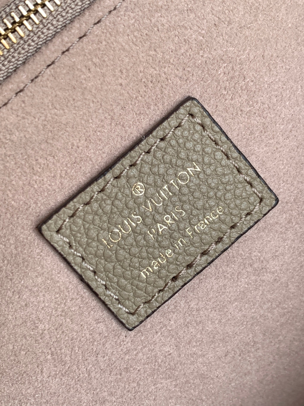 Louis Vuitton bag close-up of stitched brand label patch on taupe leather.