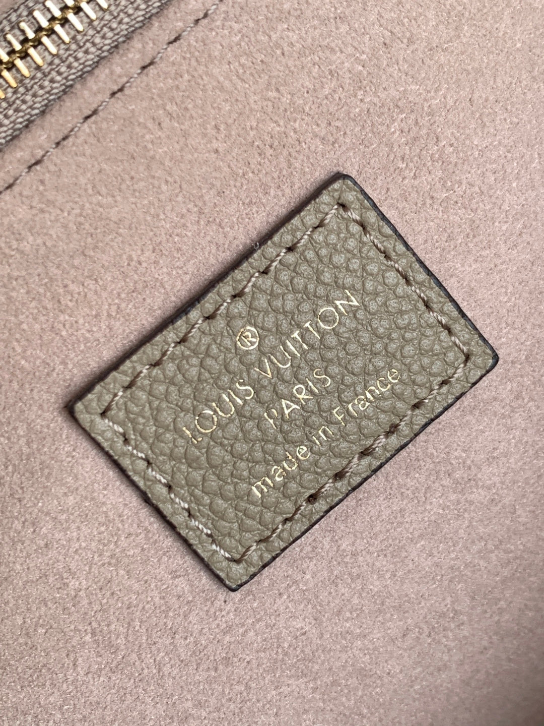 Louis Vuitton bag close-up of stitched brand label patch on taupe leather.