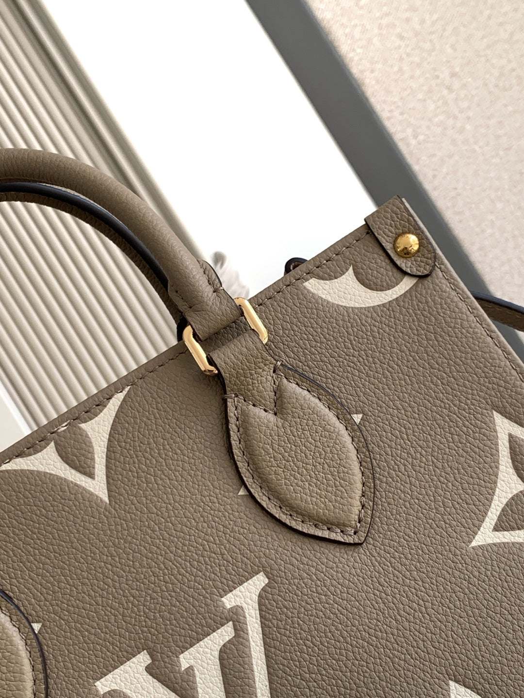 Louis Vuitton bag close-up of monogram strap patch and leather trim on gray-beige.