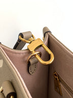 Louis Vuitton bag close-up of gold D-ring handle hardware and beige leather strap.