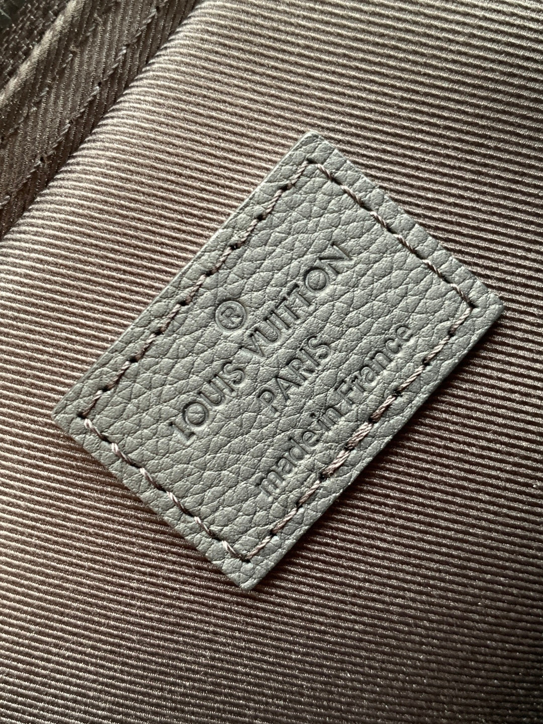 Louis Vuitton leather care label patch on dark textured bag lining