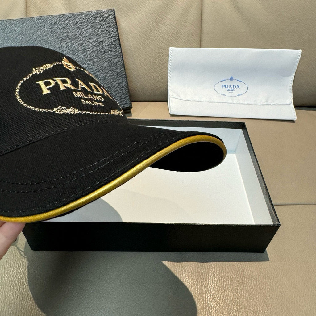 Black baseball cap close-up of curved brim with gold underside trim and logo.