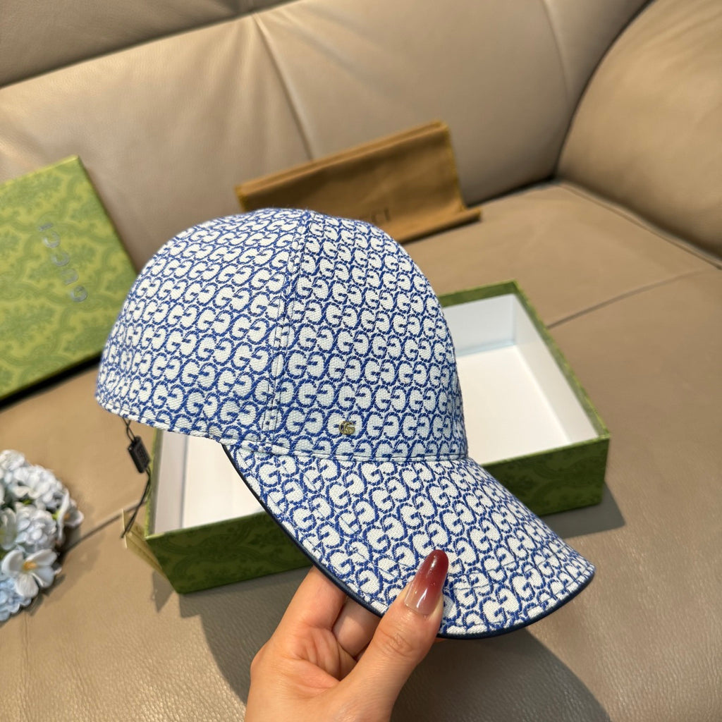 Gucci blue GG-pattern cap held by hand, curved brim and top button visible.