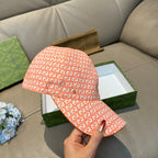 Orange GG-pattern baseball cap with curved brim, held by hand