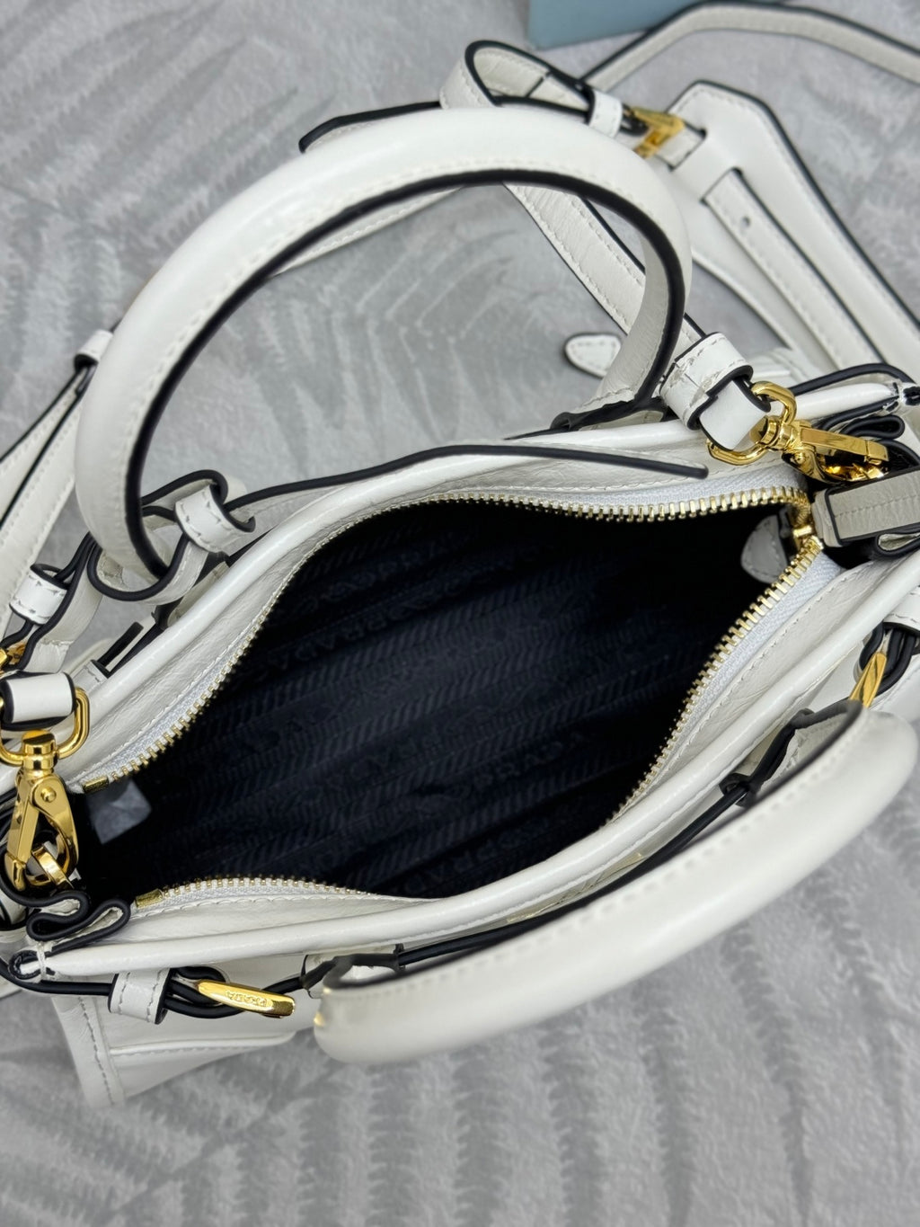 Open-top white Prada handbag interior with zipper, lining, and gold-tone hardware.