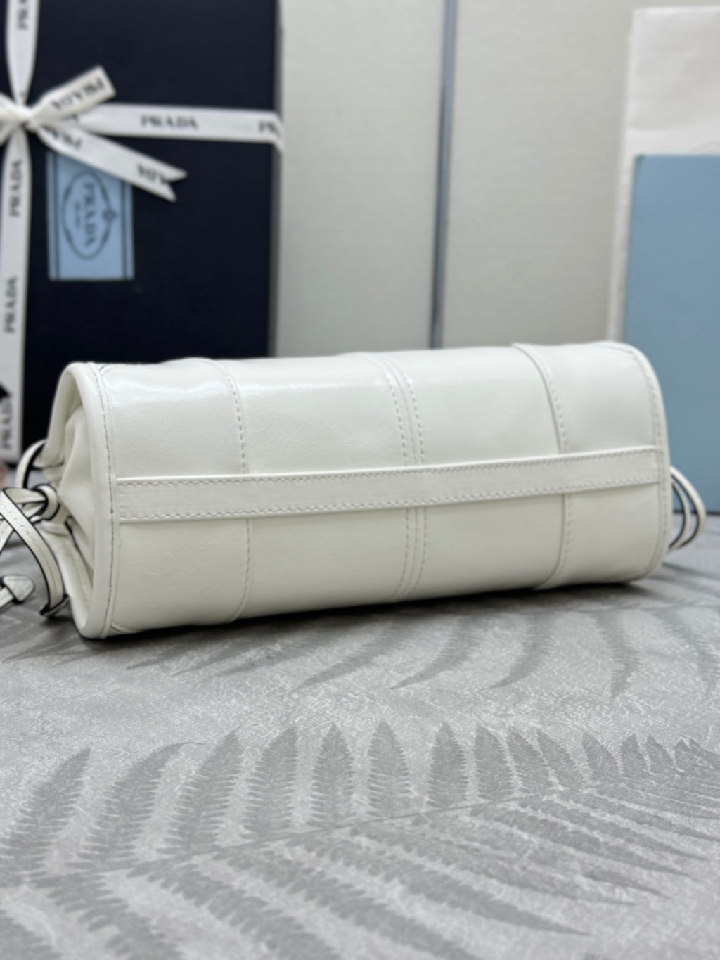 White Prada handbag with stitched front panel and short handle on top.