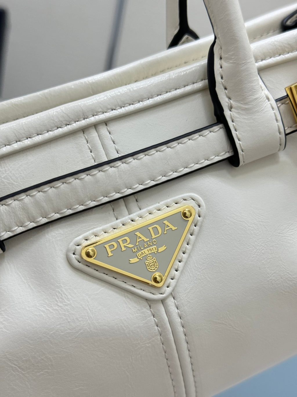 Prada white leather handbag strap detail with contrast stitching and gold logo plate.