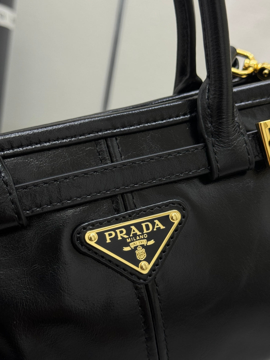 Black leather handbag close-up with gold PRADA logo plaque and stitched strap panel