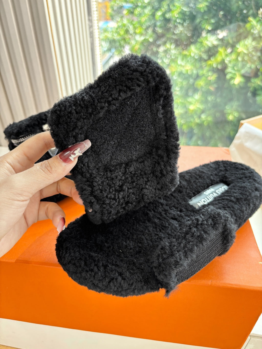 Black faux-fur mule in close-up with textured footbed and logo patch