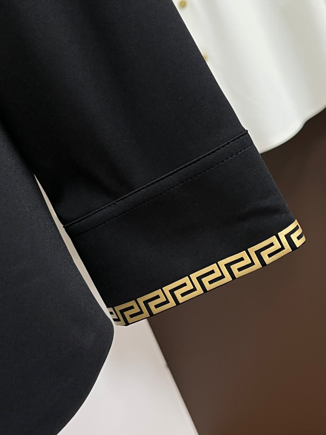Black shirt cuff with Greek-key trim band and gold medallion button