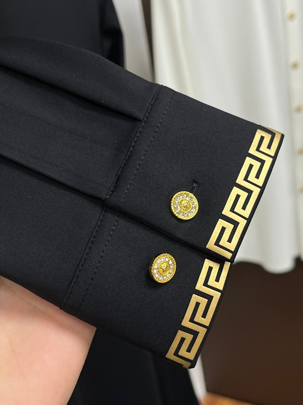 Black dress shirt sleeve cuff with gold buttons and Greek-key trim detail