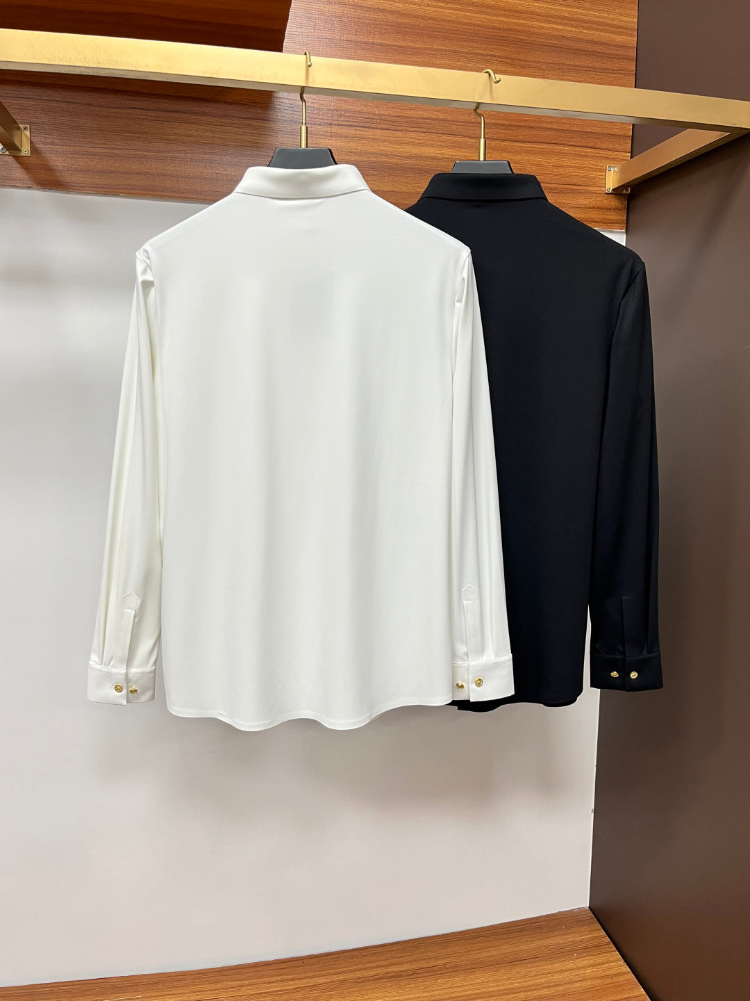 Back view of hanging white and black button-up shirts with smooth button placket