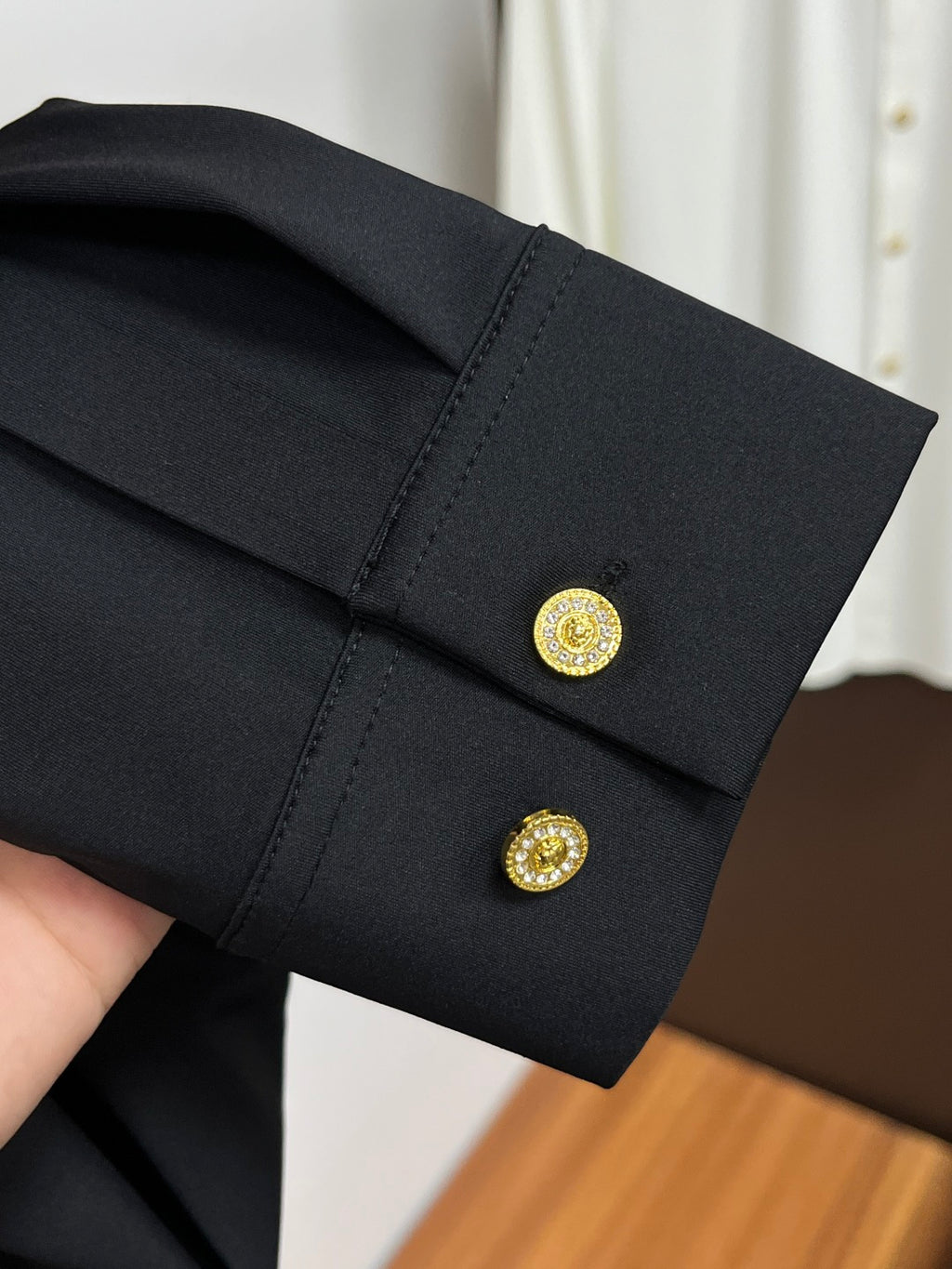 Black shirt cuff with gold button detail and small embroidered crest