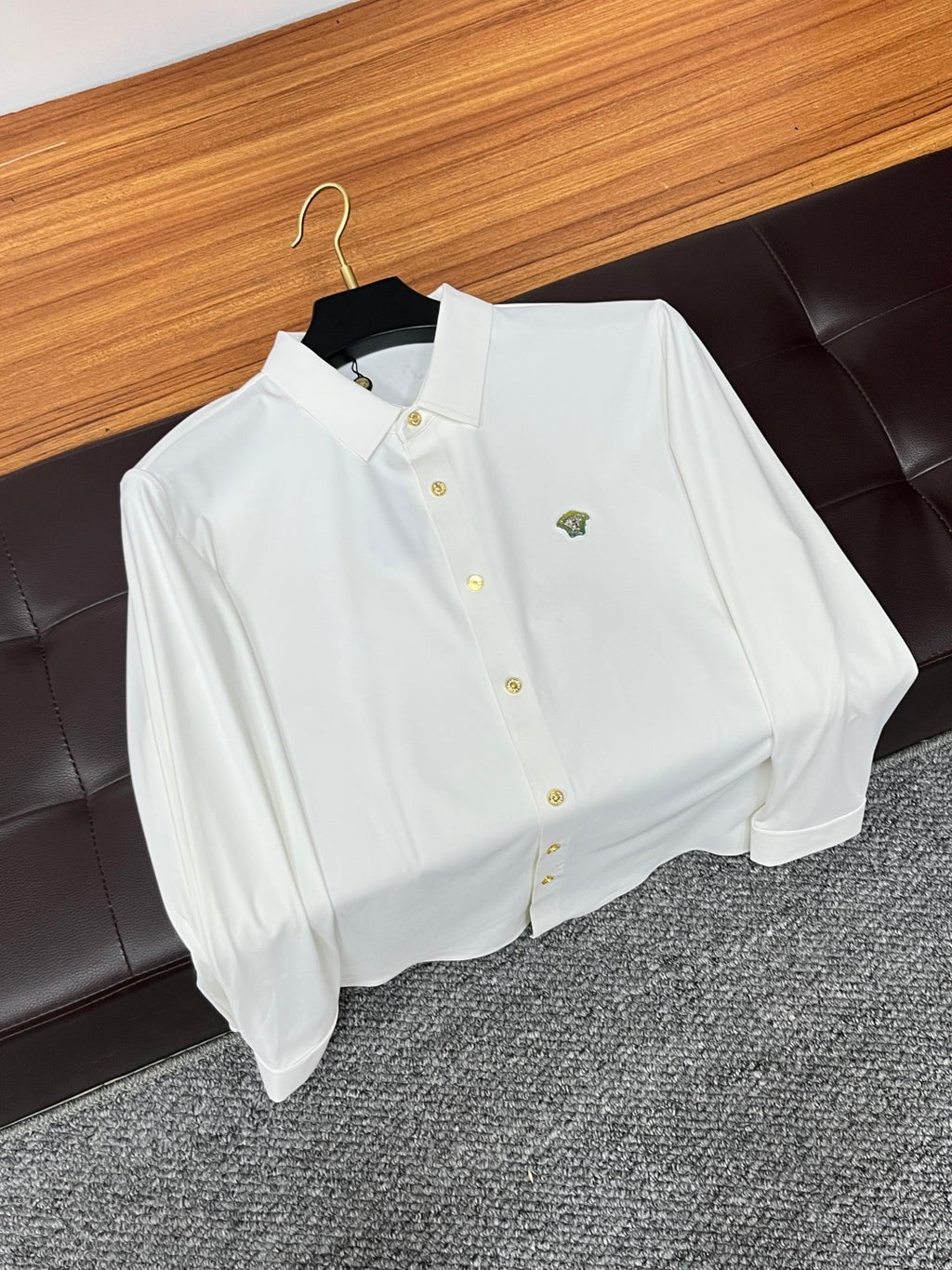 White button-up shirt with pointed collar, gold buttons, and small chest emblem