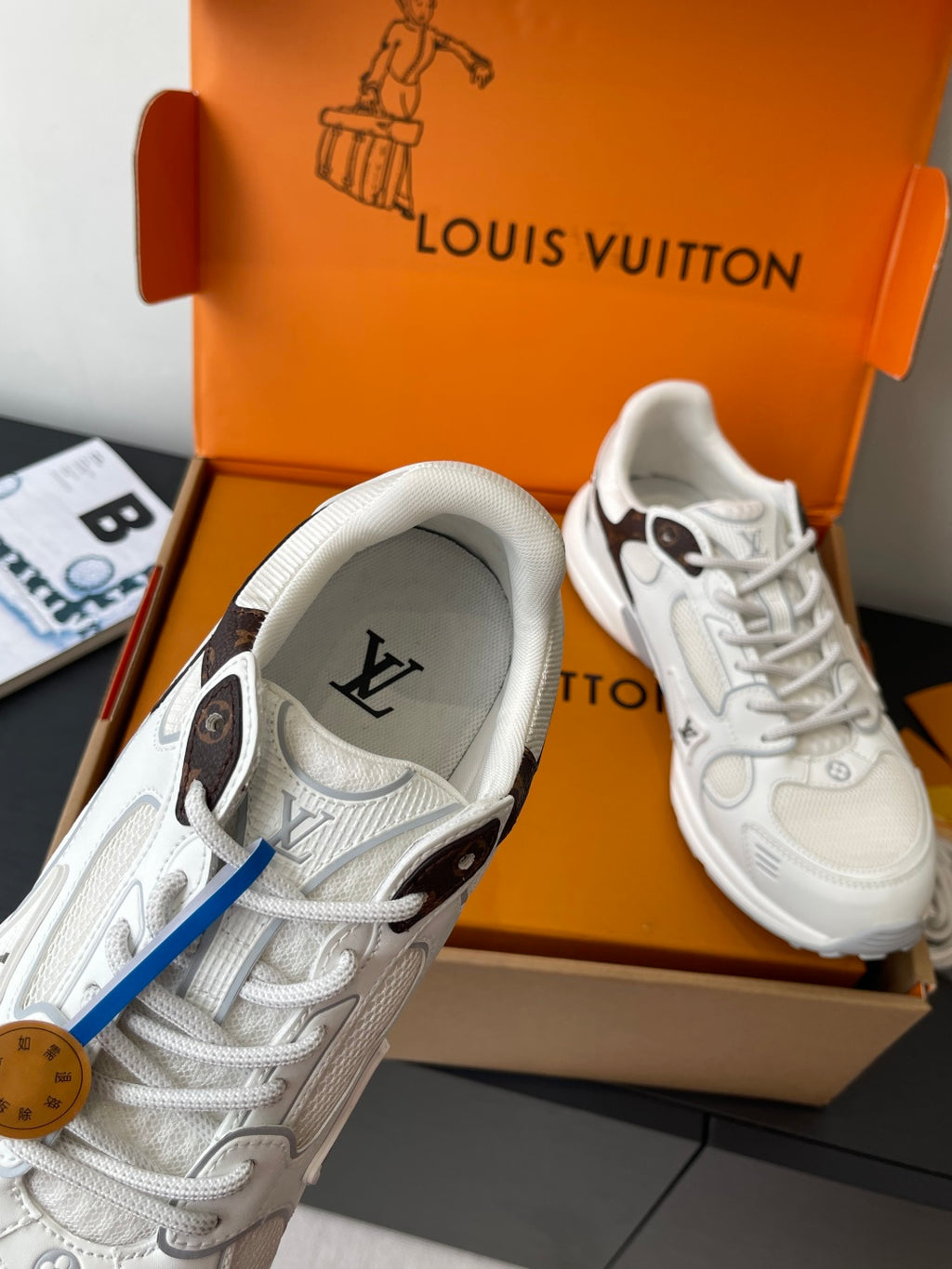 White lace-up sneaker in close-up, with textured upper and logo detail, in orange box.