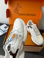 White lace-up sneaker close-up from the side, with brown emblem patch and second shoe.
