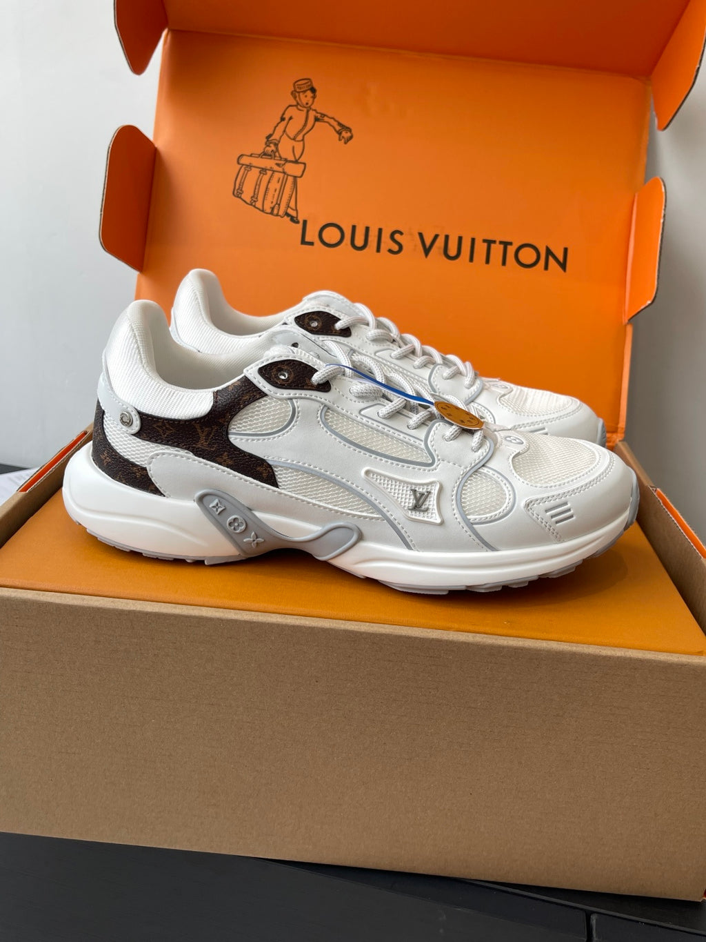 White and dark-trim lace-up sneaker, side view, placed in an open orange box.