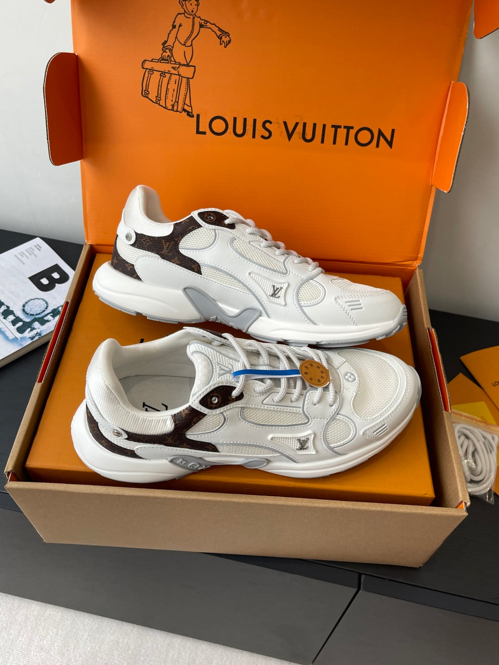White and dark-trim lace-up sneakers in an open orange box, side-by-side view.