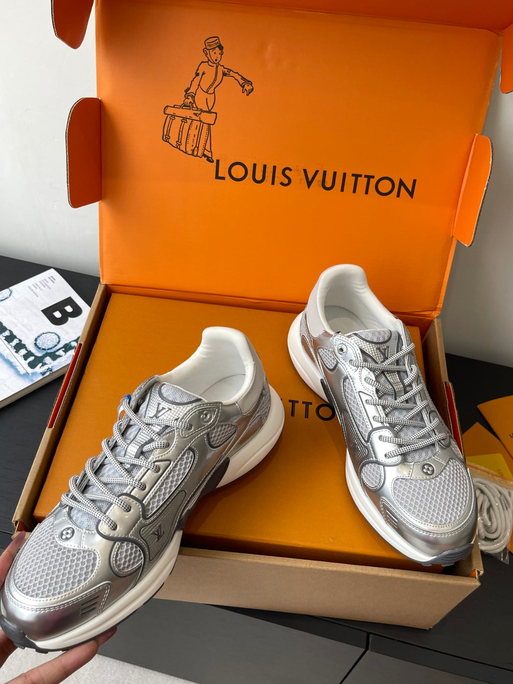 Silver lace-up sneakers with textured panels and logo accents, shown in box.