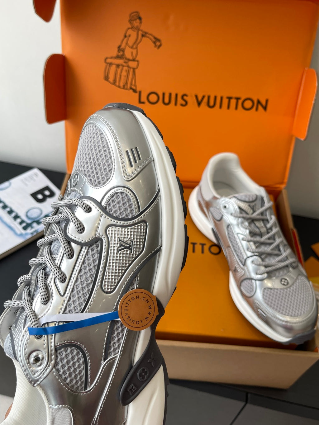 Side view of silver sneaker with raised logos and lace-up, with matching pair.