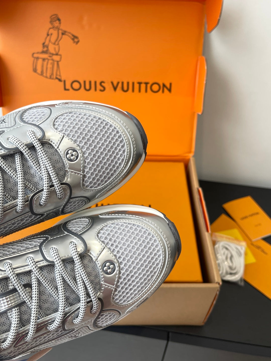 Close-up of silver sneaker toe and textured rubber outsole in orange box.