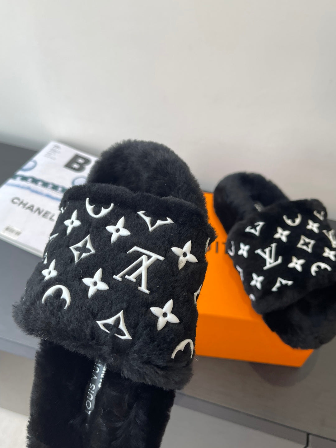 Black plush slide sandals with large white monogram motifs on the strap