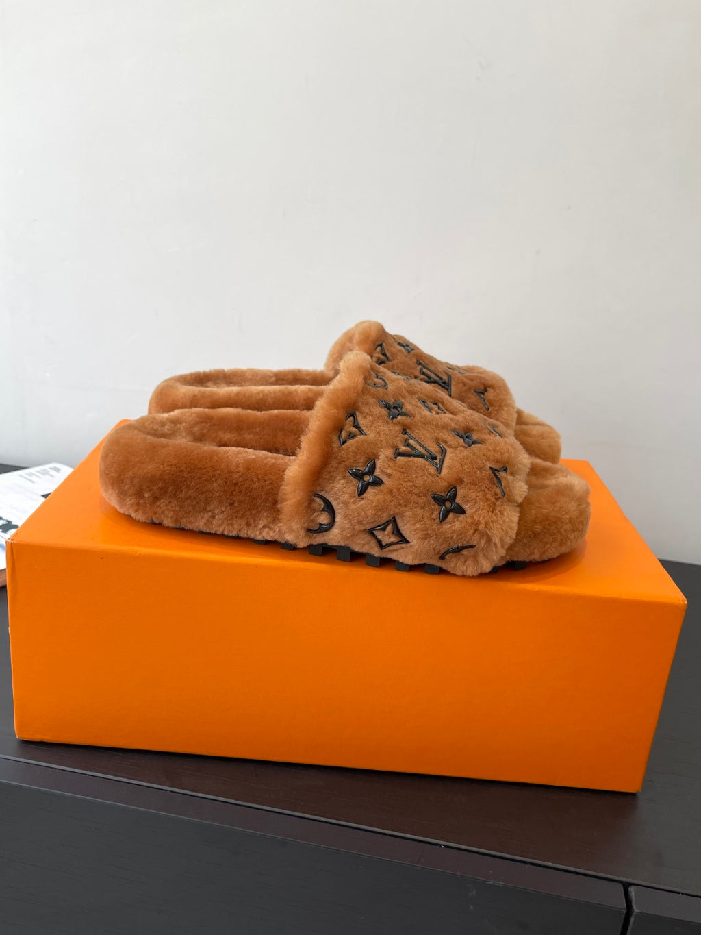 Brown plush slide sandals with dark monogram logo across the crossover strap.