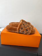 Brown plush slide sandals with dark monogram logo across the crossover strap.