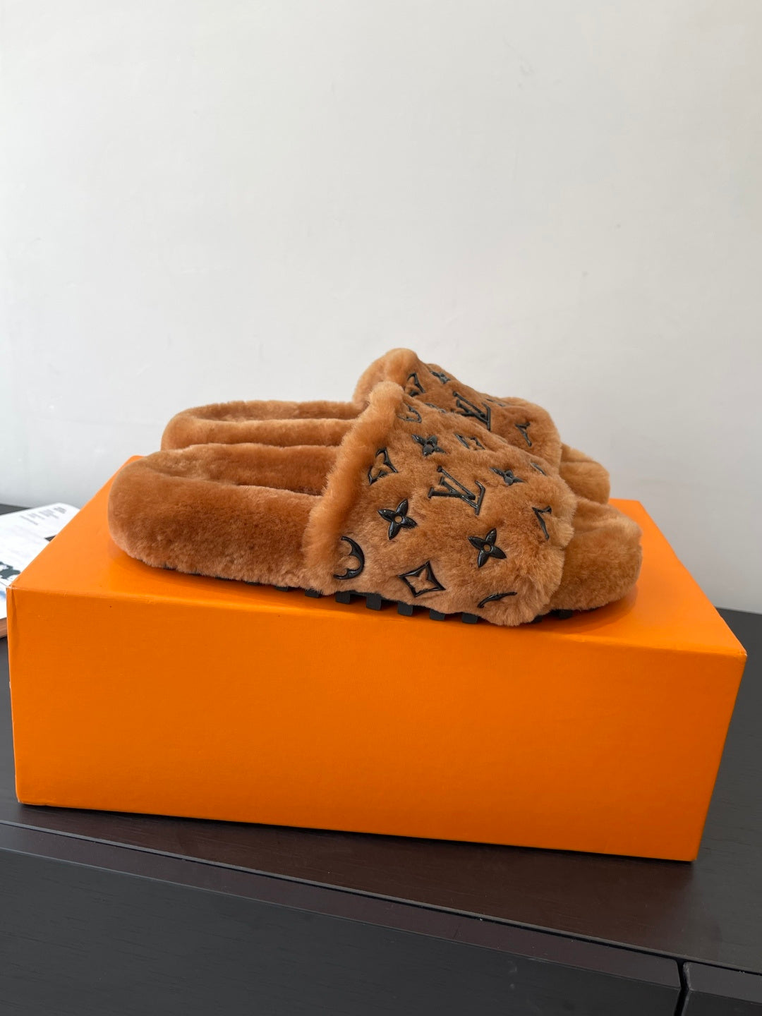 Brown plush slide sandals with dark monogram logo across the crossover strap.