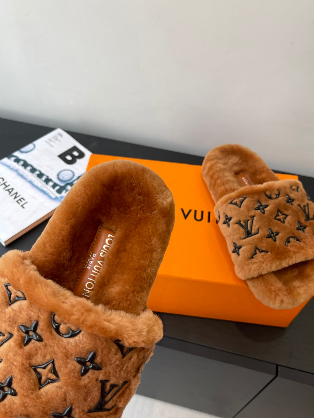 Brown fur slide sandals with dark monogram logo strap and cushioned footbed.