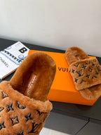 Brown fur slide sandals with dark monogram logo strap and cushioned footbed.