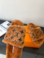 Brown fur slide sandals with dark monogram logo on the upper strap, side view.