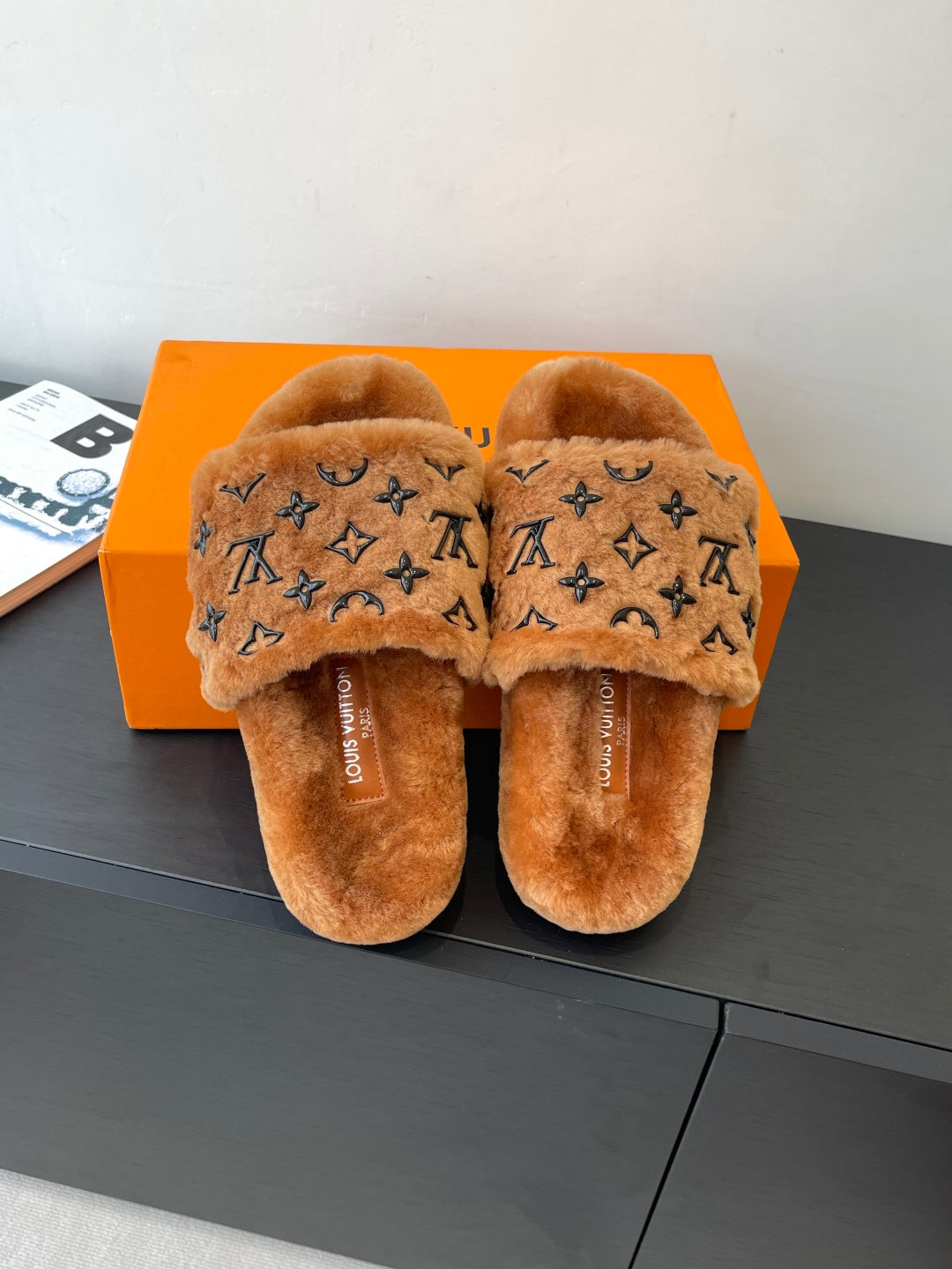 Brown plush slide sandals with dark monogram print on the crossover straps.
