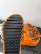 Brown fur slide sandals with dark logo outsole and cushioned upper strap.