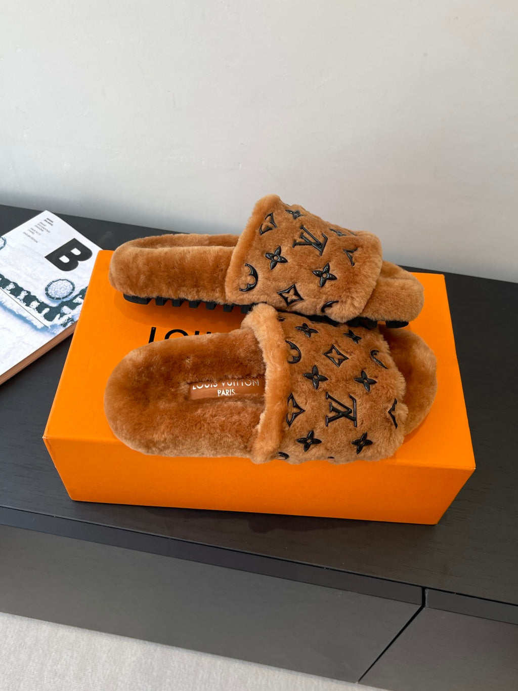 Brown fur slide sandals with dark monogram print on the crossover strap, pair shown.