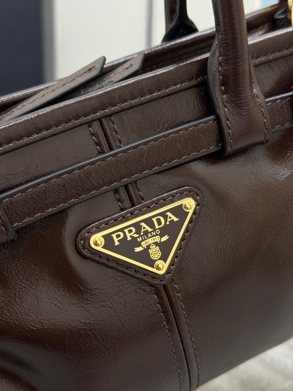 Prada brown leather bag close-up of front strap, stitching, and gold logo patch