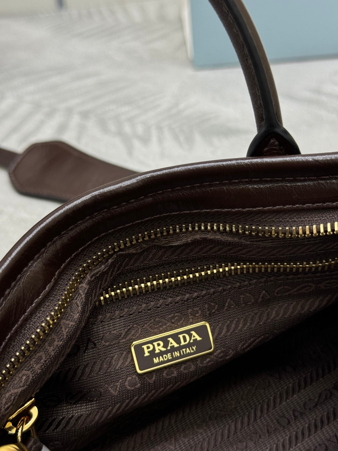 Prada brown leather bag interior close-up with gold zipper track and logo patch