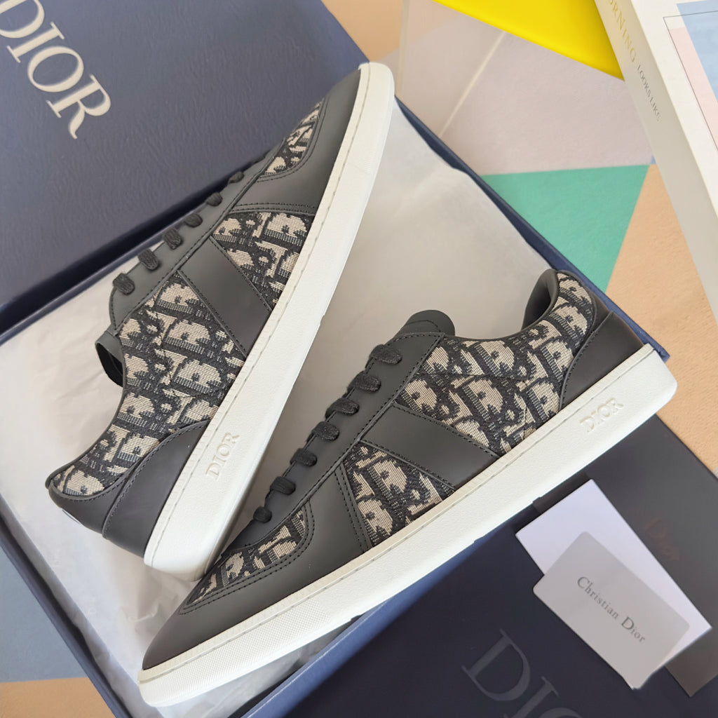 Low-top sneakers, dark gray leather and Dior monogram uppers, black laces, chunky white sole.