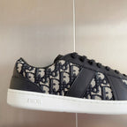 Low-top sneaker close-up, Dior monogram fabric with dark gray leather trim, black laces.