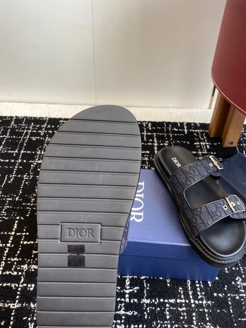 Dior sandal outsole with ridged tread and dark blue patterned strap, on blue box