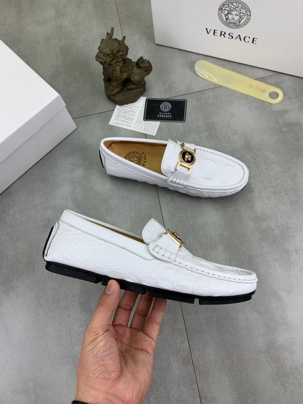White slip-on loafer on a hand, gold buckle and tan interior visible
