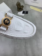 White loafer close-up with gold emblem buckle and textured leather upper