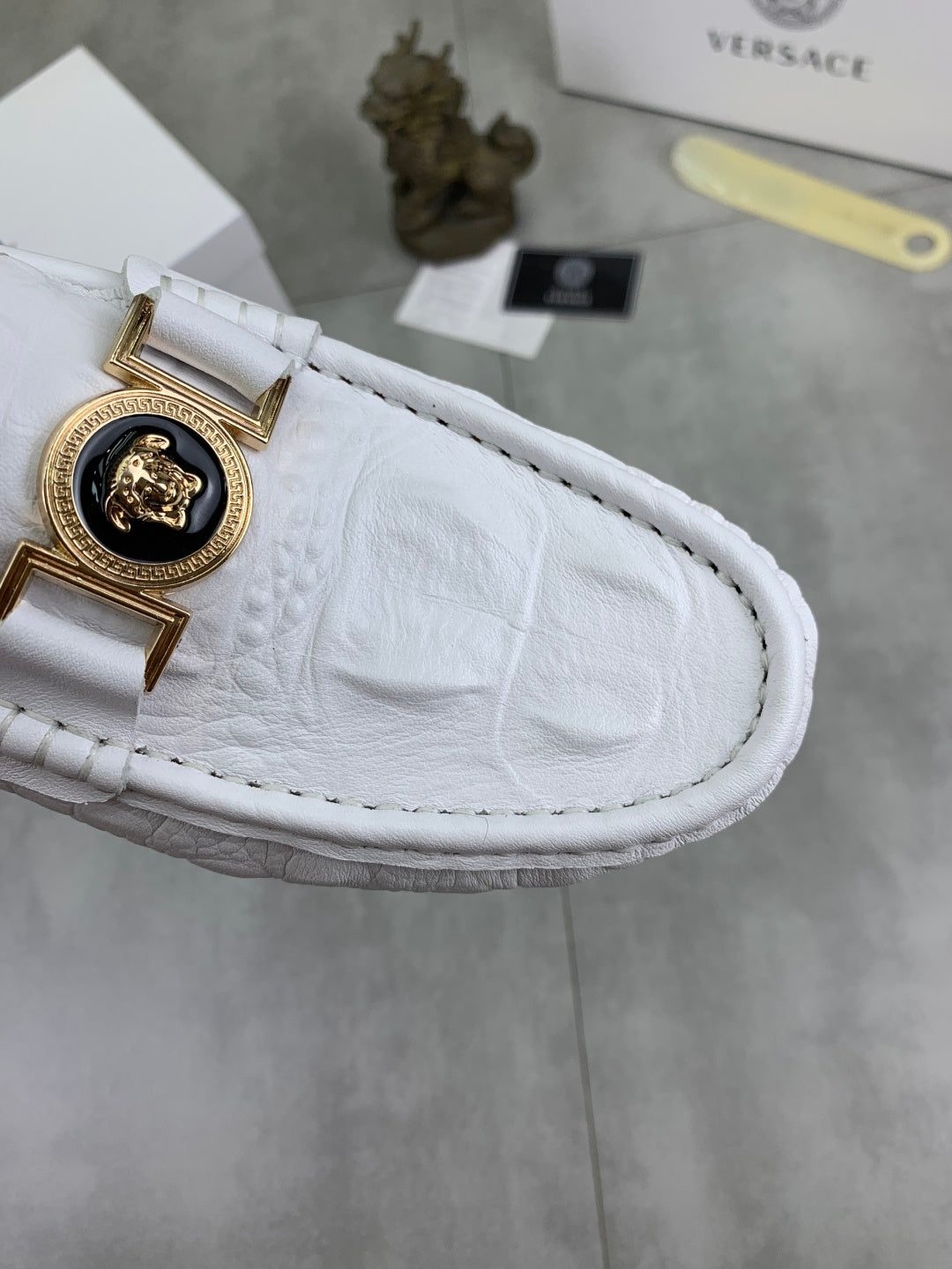 White loafer close-up with gold emblem buckle and textured leather upper