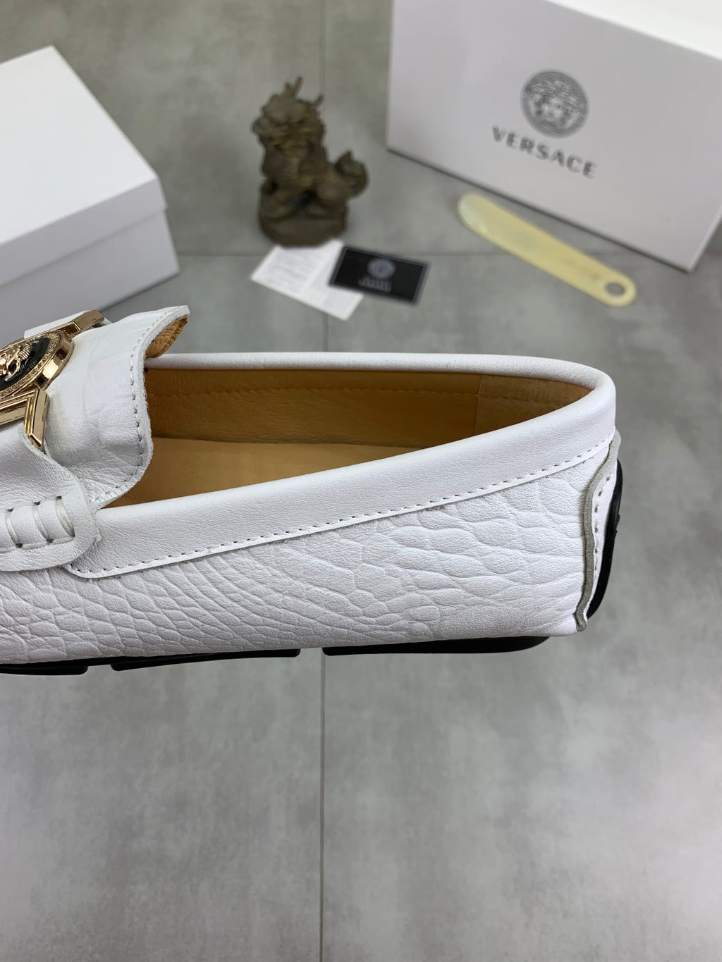 White slip-on loafer side view with gold buckle and black sole trim