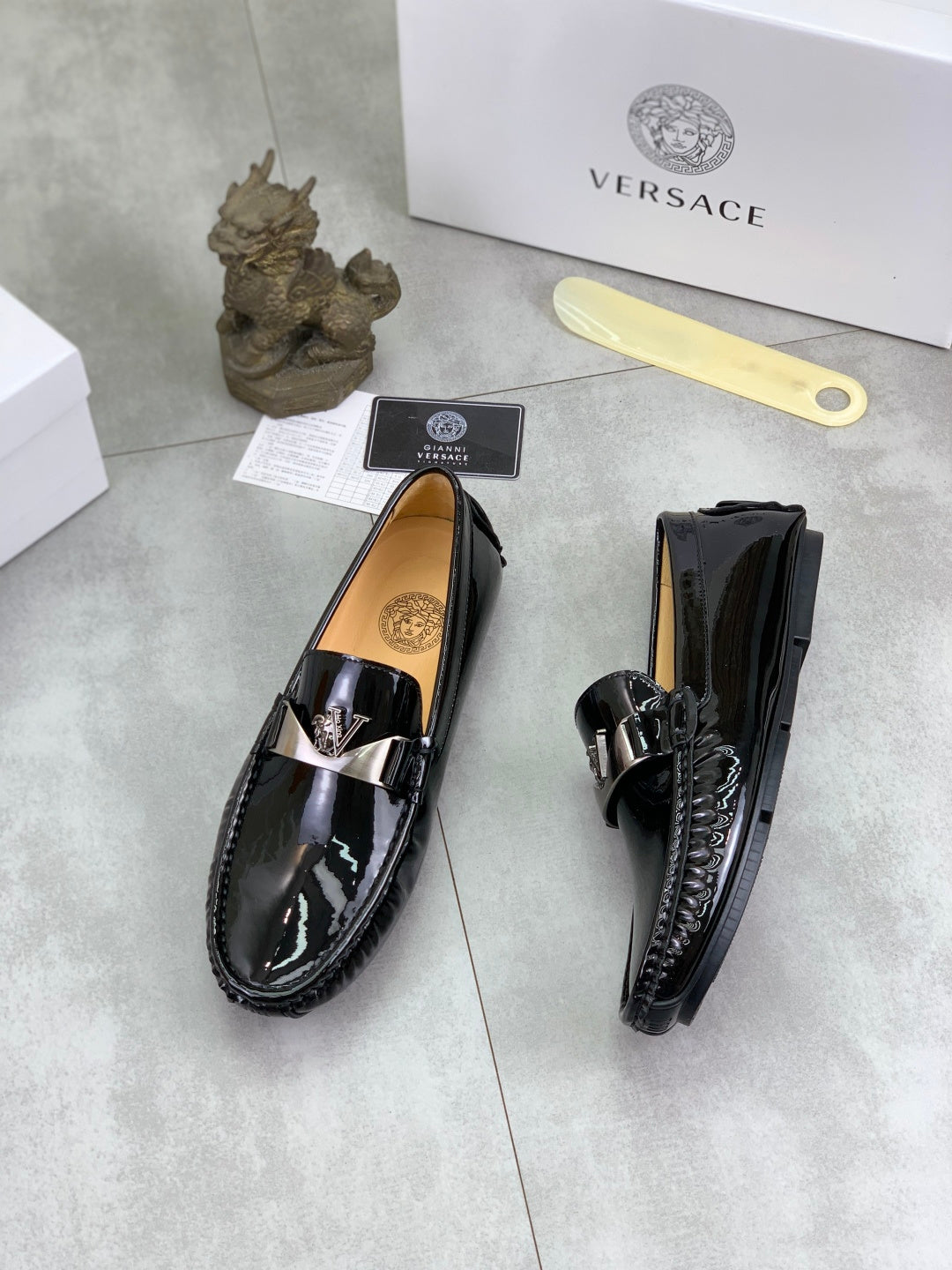 Black patent leather loafers with metal front emblem and textured side stitching
