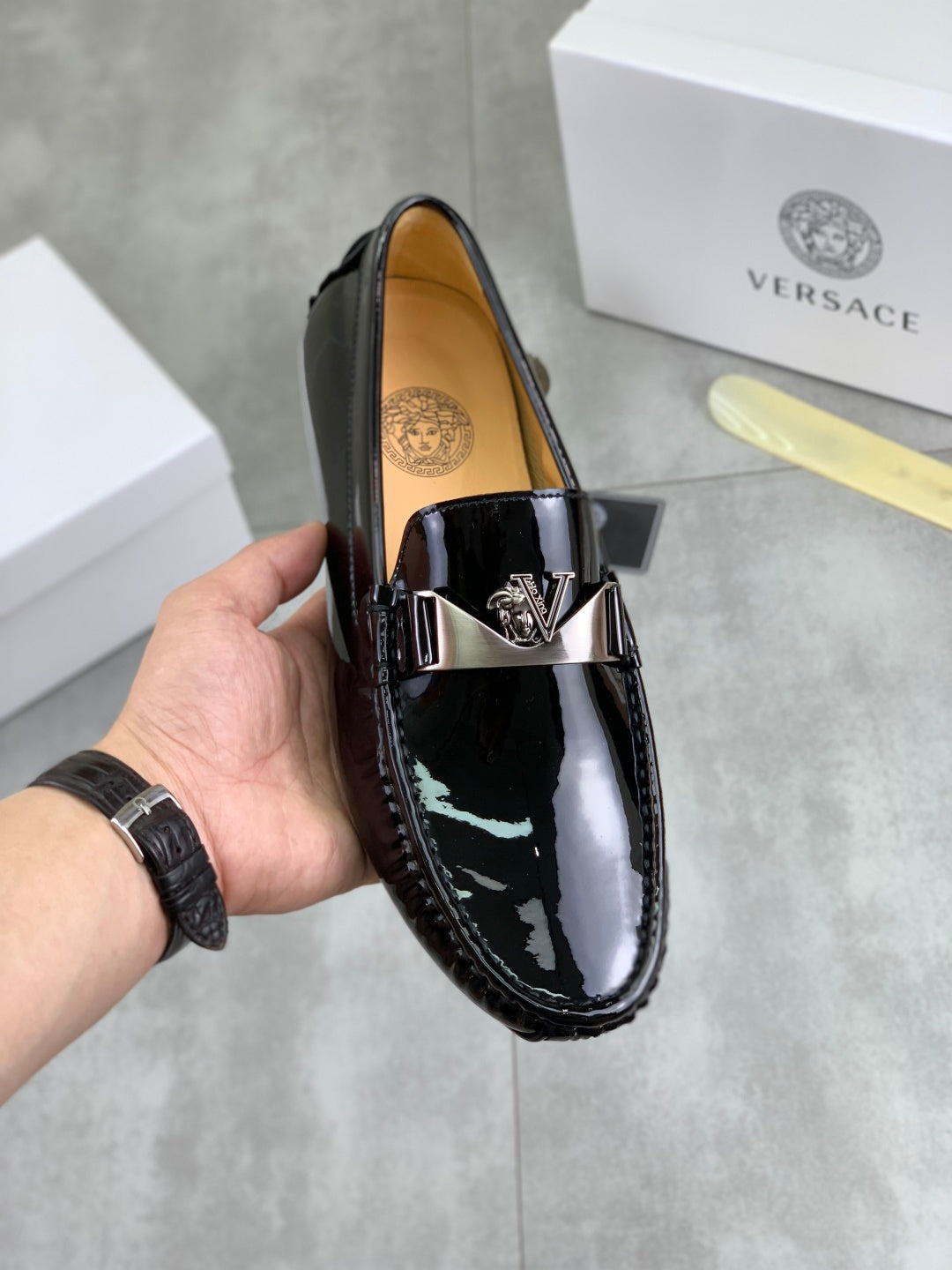 Black patent leather loafer with metal emblem strap detail and stitched apron