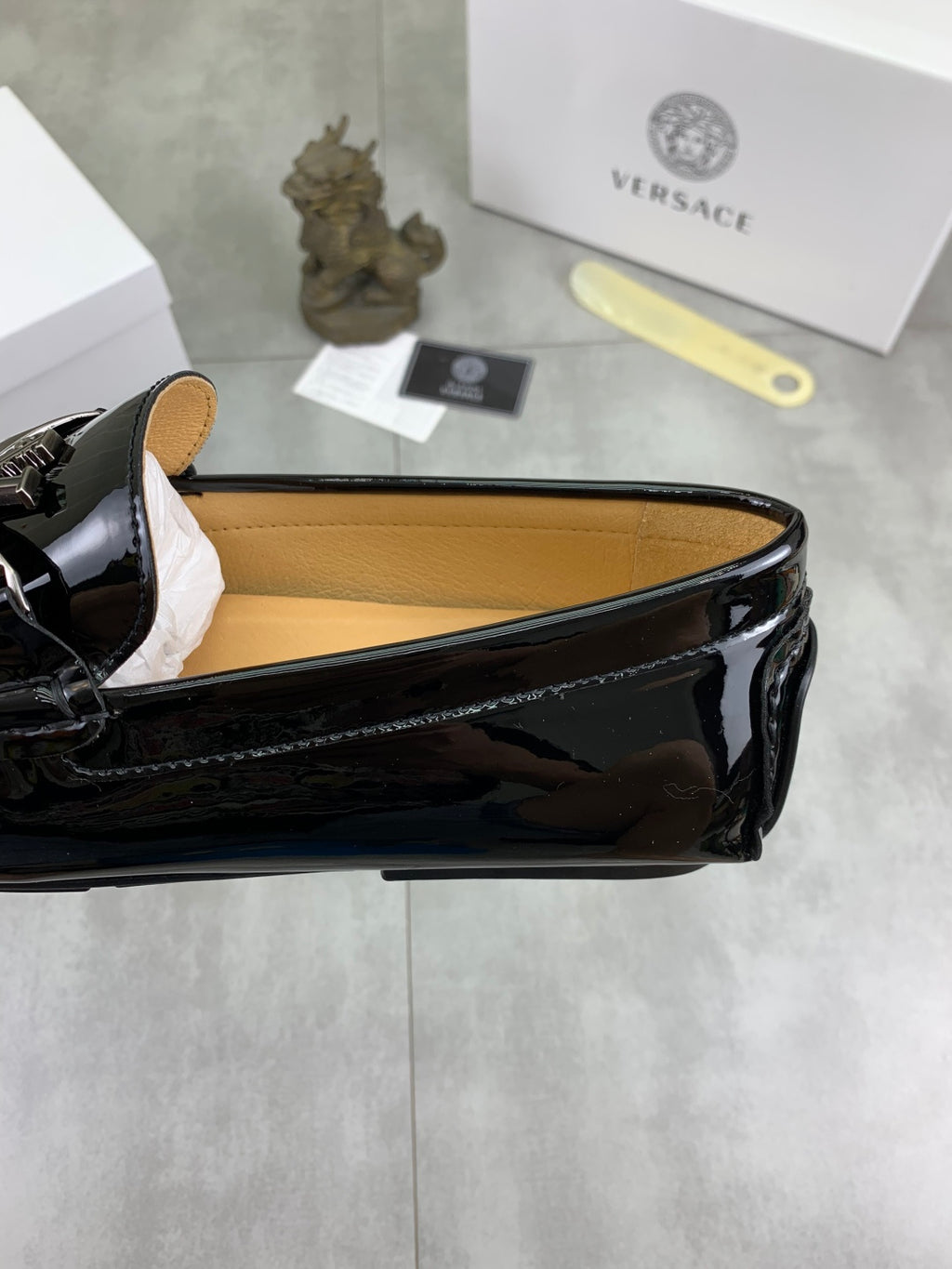 Black patent leather loafer showing interior lining and decorative emblem front
